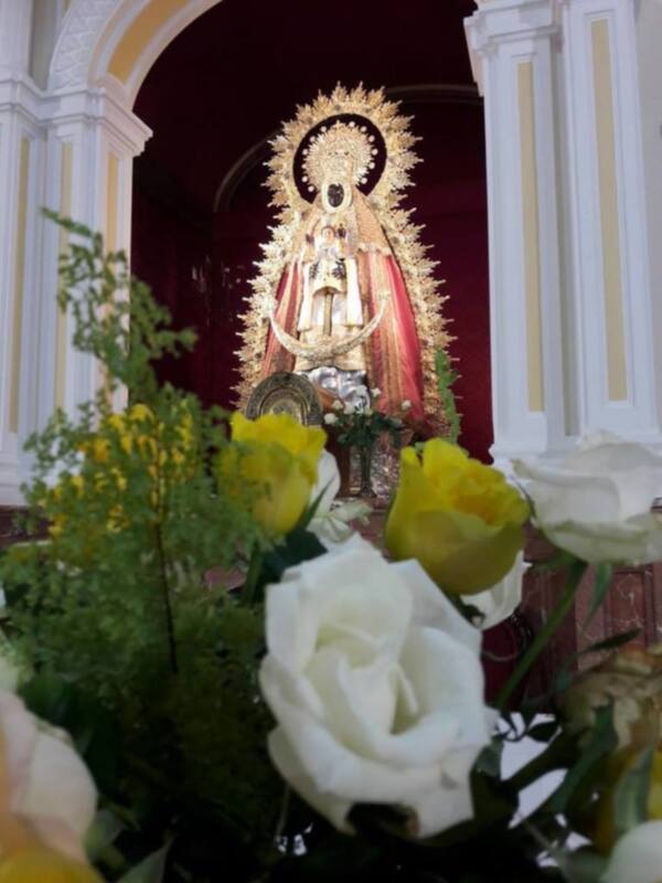 Venerada imagen de la Virgen del Carmen en un altar adornado con flores blancas y amarillas.