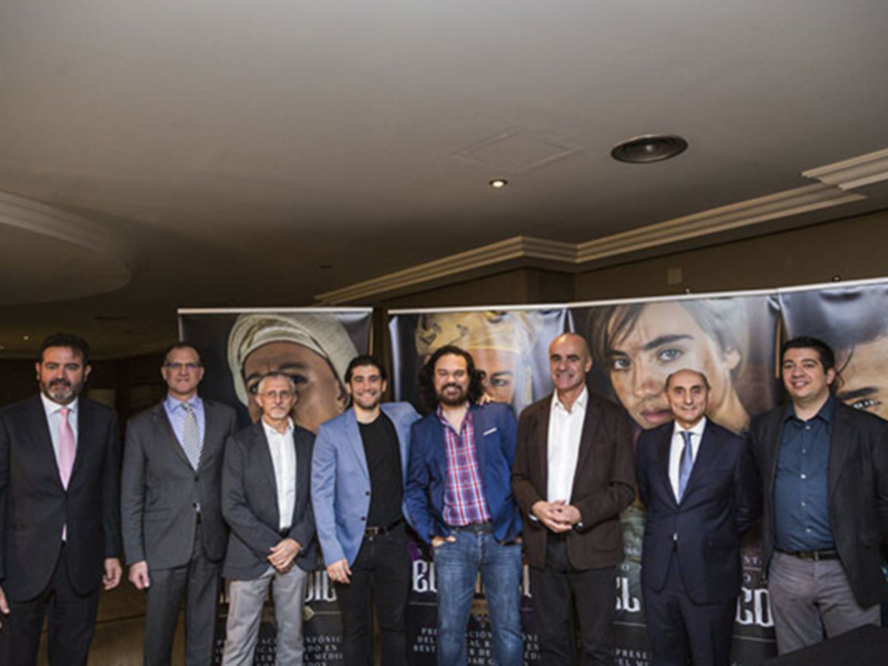 Grupo de hombres en trajes posando en un evento formal con carteles en el fondo.