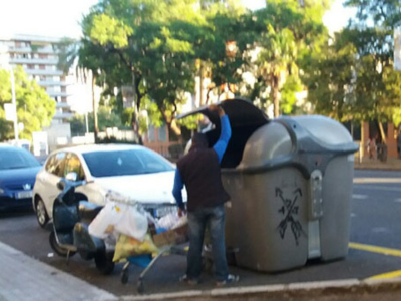 Persona recogiendo basura en contenedores de reciclaje urbano.