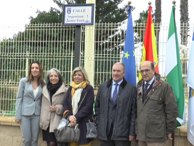 Grupo de personas frente a un letrero con la inscripción 'CALLE Ingeniero Jaime Font' y banderas en el fondo.