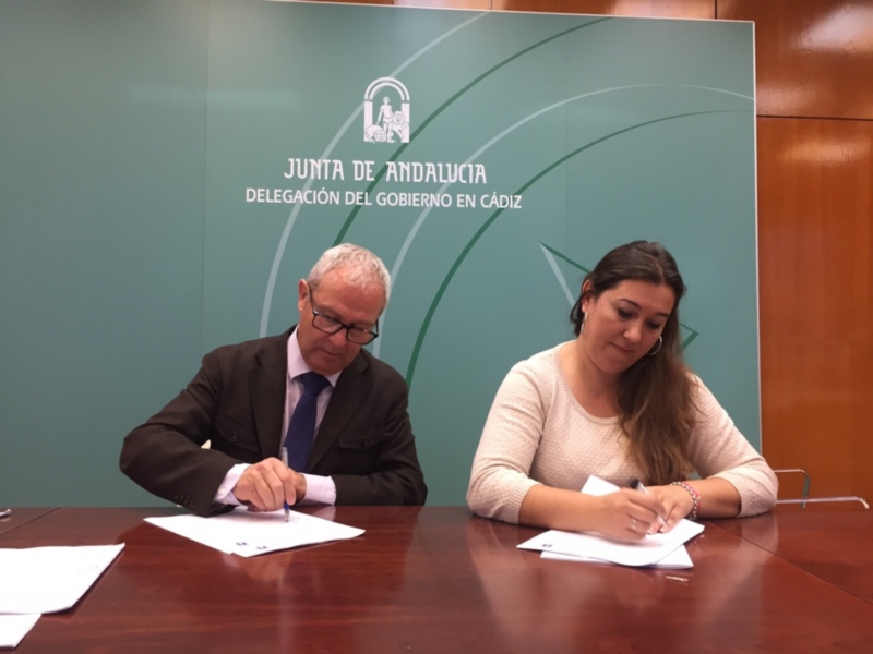 Un hombre y una mujer firmando documentos en una mesa con un fondo de la Junta de Andalucía en Cádiz.