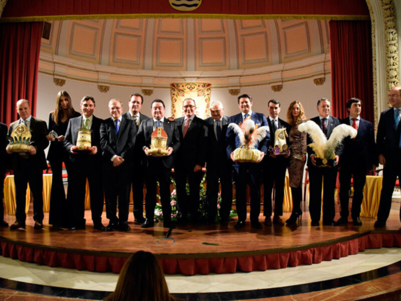 Gala de premiación en un teatro con participantes en trajes formales sosteniendo trofeos y galardones.