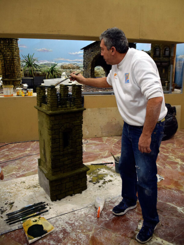 Hombre trabajando en la pintura de una estructura de piedra en un taller de modelismo.