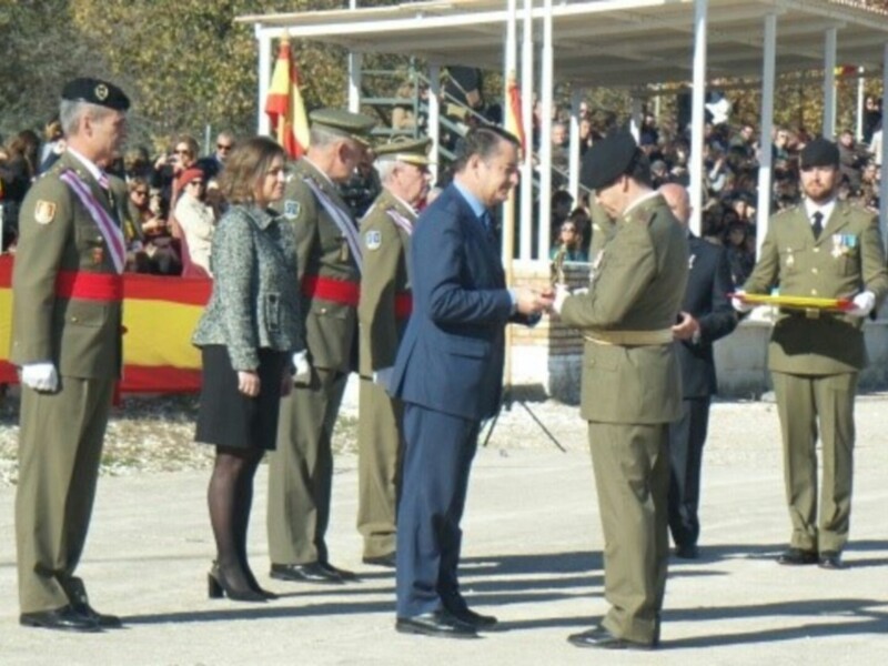 Entrega de una medalla en una ceremonia militar con personal civil y militar presente.