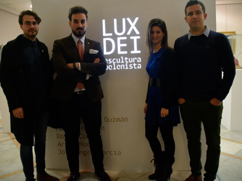 Cuatro personas posan juntas en una exposición de arte, con el cartel 'LUX DEI' y 'Escultura' en el fondo.