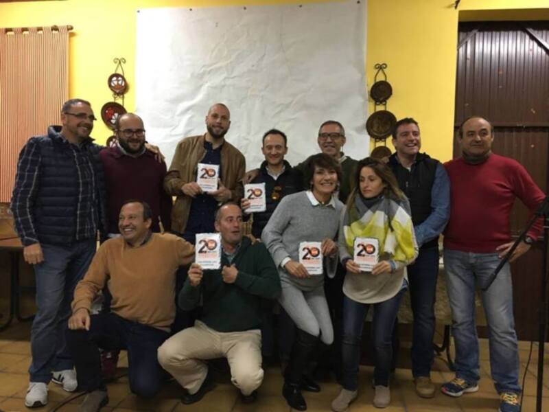 Celebración del 20º aniversario con un grupo de personas sonrientes y sosteniendo placas con el número 20.