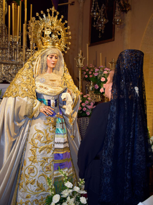 Procesión de la Virgen con devotos en una iglesia decorada con flores y candelabros.