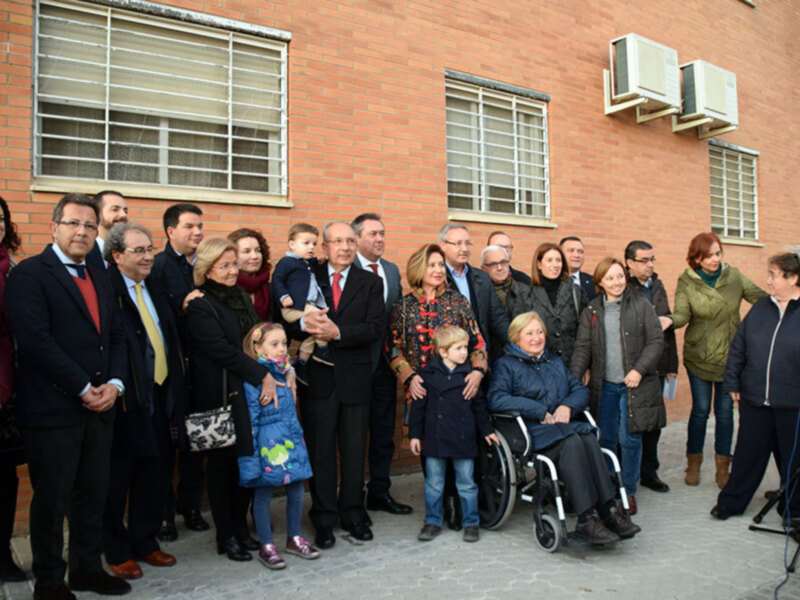 Grupo de personas posando frente a un edificio de ladrillo rojo, con una persona en silla de ruedas y un niño pequeño en brazos de una mujer.