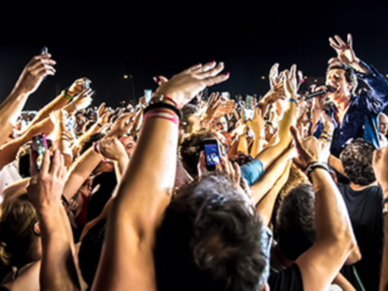 Fotografía de un concierto nocturno con el público levantando las manos en el aire, capturando el entusiasmo y la energía del evento.