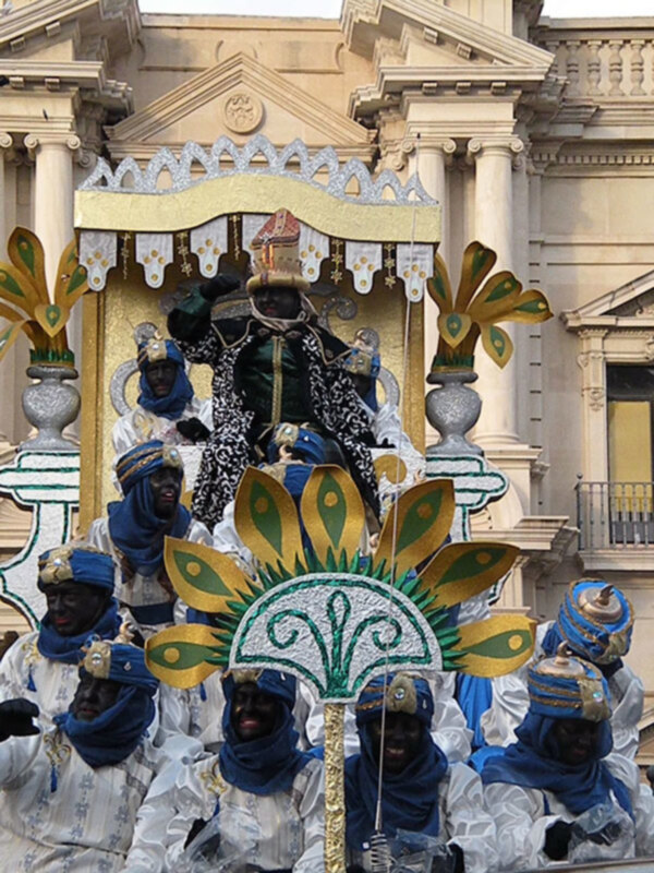 Desfile de carnaval con figuras vestidas con trajes tradicionales y sombreros ornamentales en un escenario festivo.