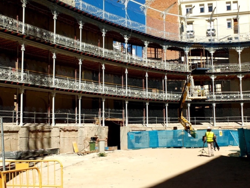 Interior de un edificio en construcción con estructura histórica y trabajador en el suelo.