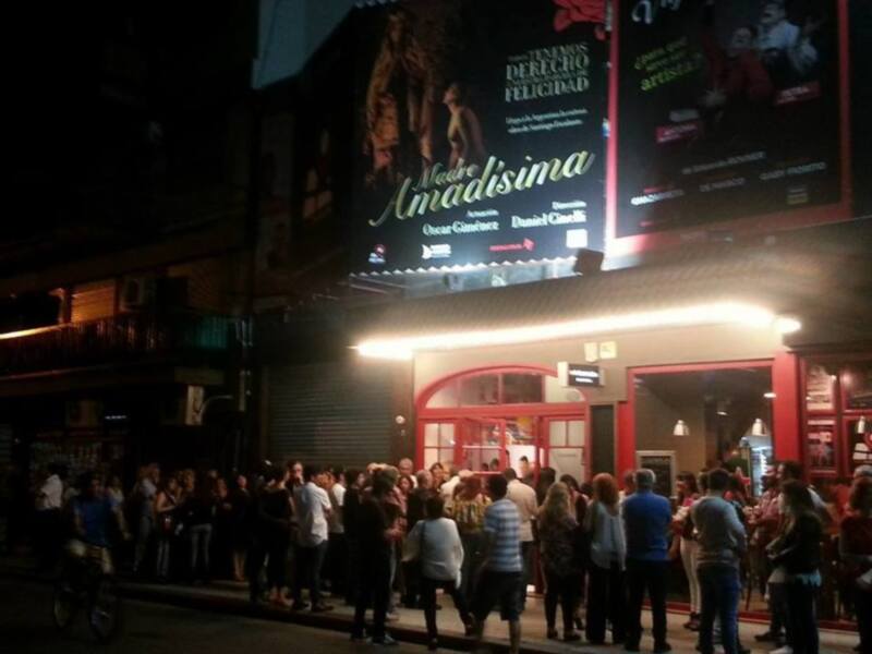 Folleto de la obra 'Madre Amadisima' en una calle nocturna con una gran afluencia de personas.