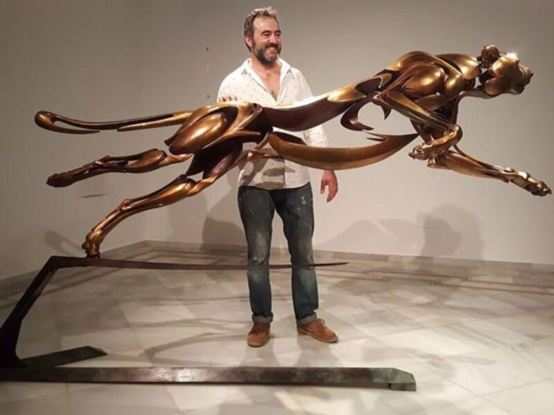 Escultor junto a su obra de bronce en movimiento fluido.