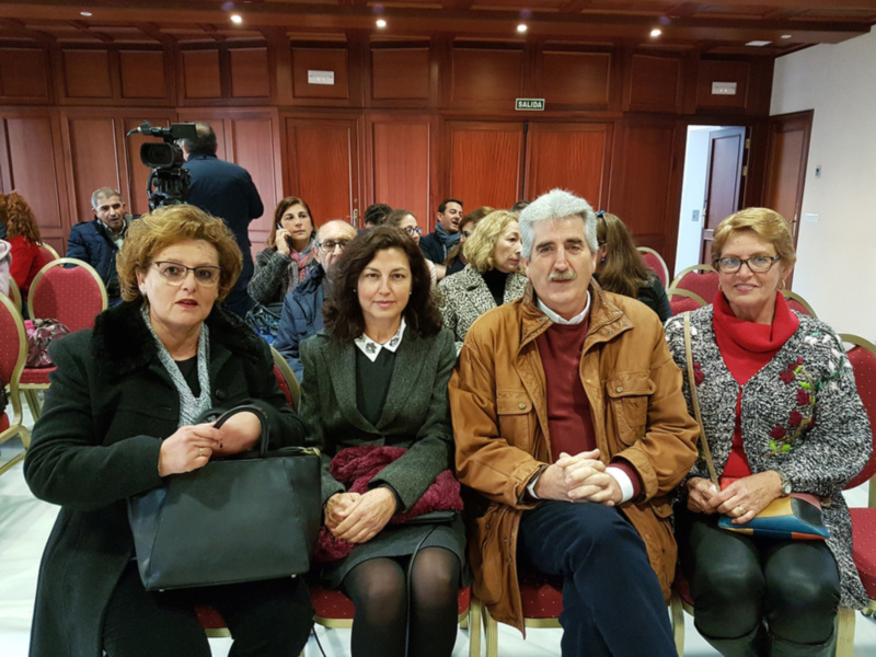 Una reunión de negocios en un salón de conferencias con personas sentadas en sillas rojas y una cámara de video en el fondo.