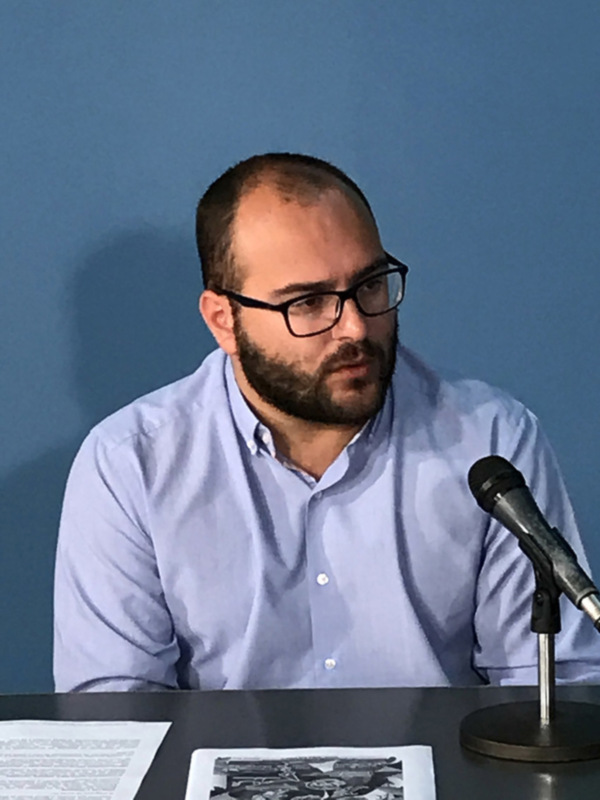 Hombre con barba y gafas hablando en una conferencia de prensa.