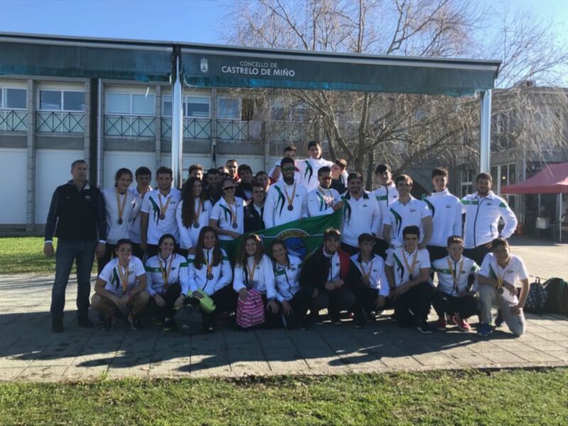 Equipo de atletismo celebrando su victoria en el concello Castrelo de Miño, con medallas en el cuello y bandera de club en el centro.