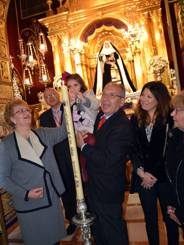 Familia celebrando una misa en una iglesia ornada, con una mujer sosteniendo una vela iluminada.