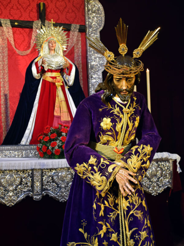 Representación de Jesús Nazareno con una corona de espinas y una Virgen de la Soledad en el fondo, durante una procesión religiosa.