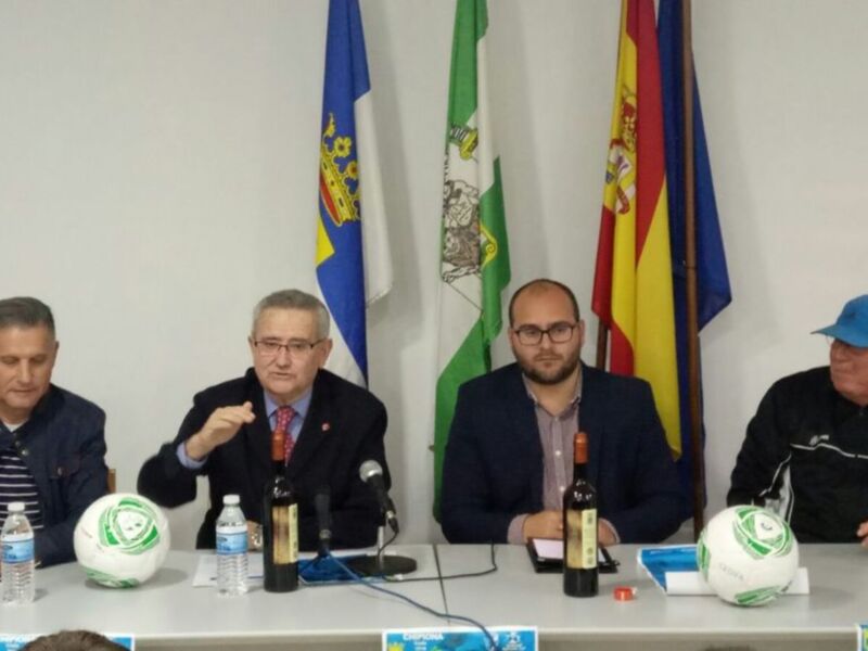 Tres hombres sentados en una mesa con banderas en el fondo, posiblemente en una conferencia de prensa o reunión oficial.