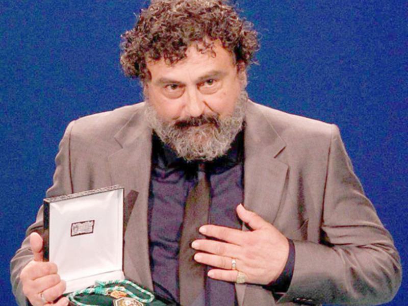 Persona con barba y cabello rizado mostrando una medalla en una caja abierta.