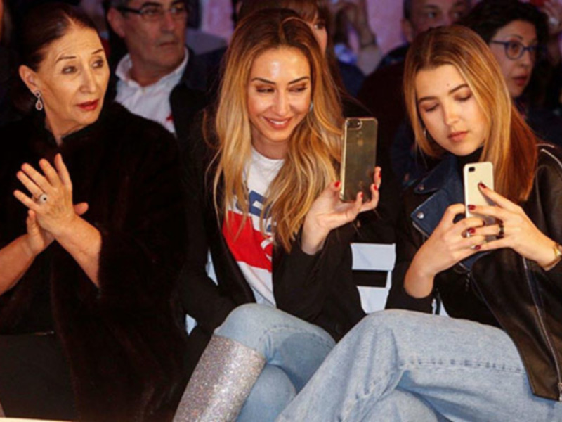 Tres personas sentadas en un evento, dos de ellas están usando sus teléfonos inteligentes.