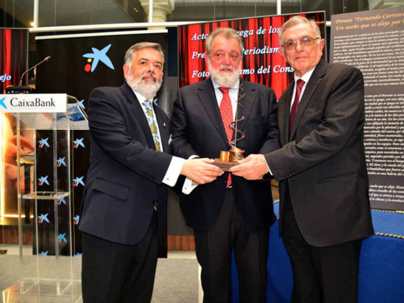 Premio "Fernando Carrasco" Año 2023. Tres hombres en trajes presentan un trofeo en un evento formal.