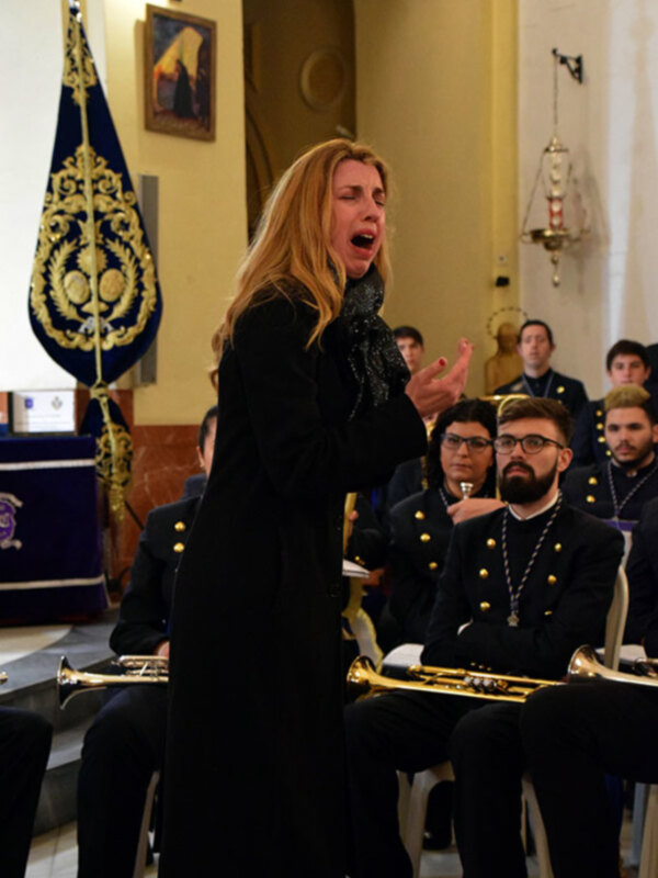 Una mujer dirige una banda de música en un entorno formal, posiblemente una ceremonia o concierto.