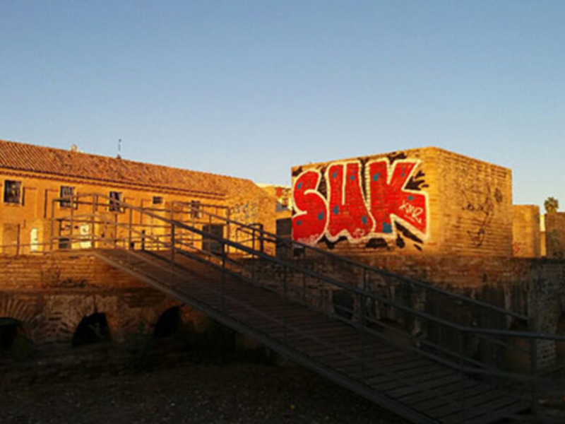 Puente antiguo con grafitis en el muro, iluminado por el sol en la parte superior.