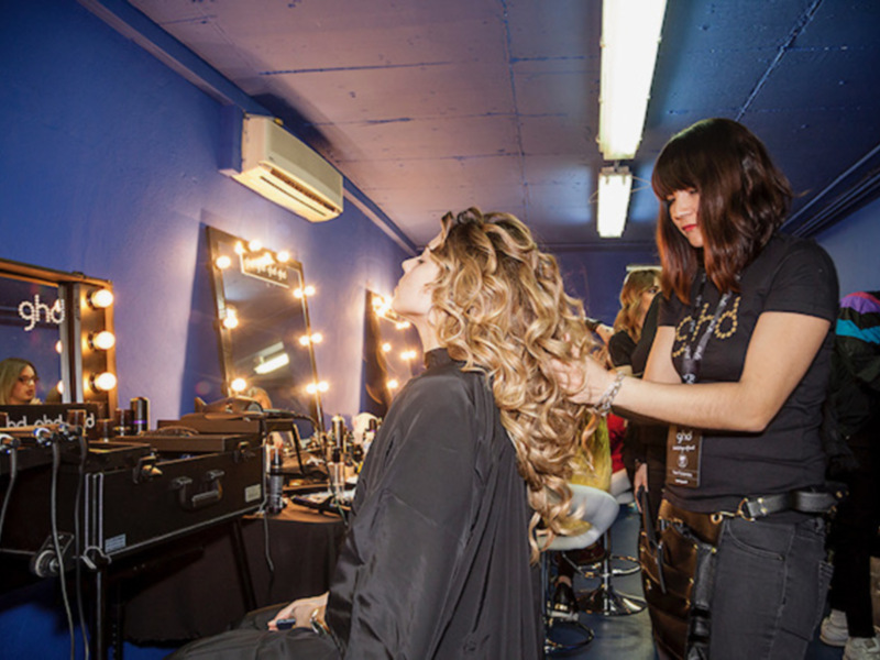 Estilista trabajando en el cabello de una cliente en un salón de belleza con luces de espejo iluminadas.