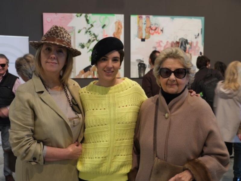 Tres personas sonrientes posando juntas en una exposición de arte.