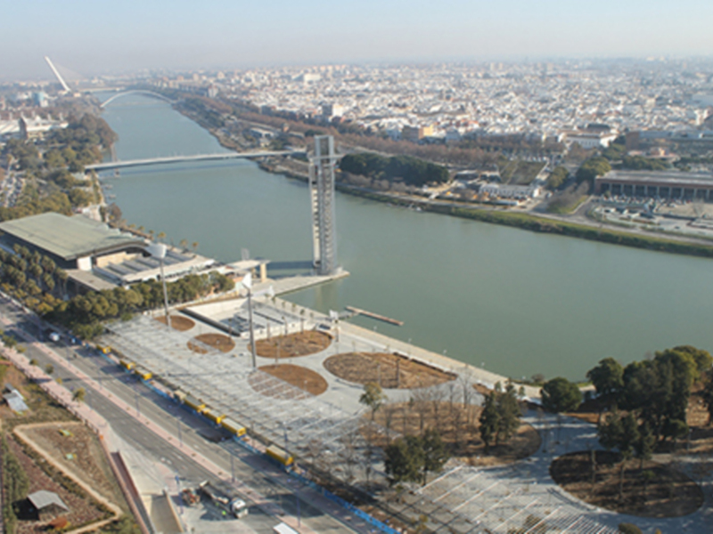 Vista aérea de una ciudad con un río y un puente en primer plano, con edificios y vegetación alrededor.