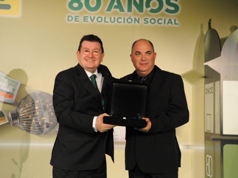 Celebración de 80 años de evolución social: dos hombres en trajes presentan un premio en un evento formal.