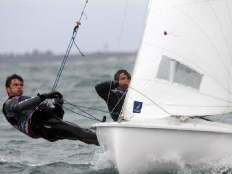 Dos regatistas en acción en un velero blanco navegando en aguas abiertas.