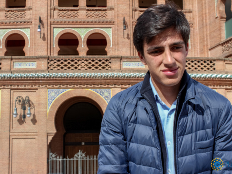 Joven posando frente a un edificio histórico con arcos y detalles decorativos.