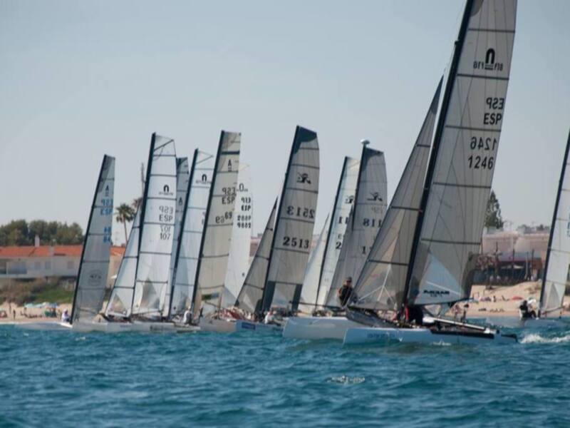 Competidores en una regata de vela en el mar, con velas numeradas y barcos navegando juntos.
