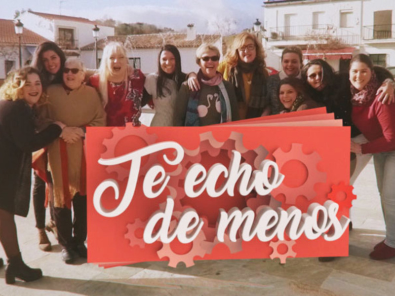 Grupo de mujeres sonrientes en un pueblo blanco, con el texto 'Te echo de menos' en el fondo rojo.