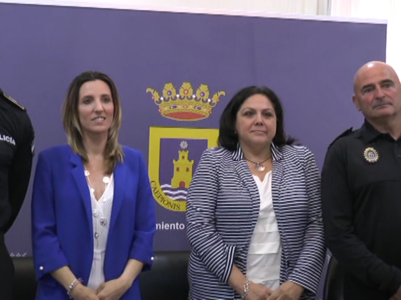 Tres personas, dos de ellas con uniformes policiales, posan frente a un fondo azul con el escudo de la Policía Nacional de España, junto a una bandera española. La escena sugiere una conferencia de prensa o anuncio oficial.