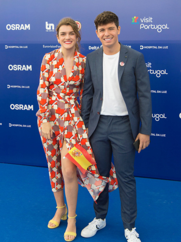 Dos personas sonrientes posando juntos en un evento con fondo azul y logos de patrocinadores como OSRAM y EurovisionFans.