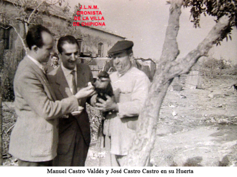 Hombre en traje intercambia con otro en uniforme en un entorno rural, posiblemente un huerto, con texto en español sobre cronista de la villa de Chipiona.