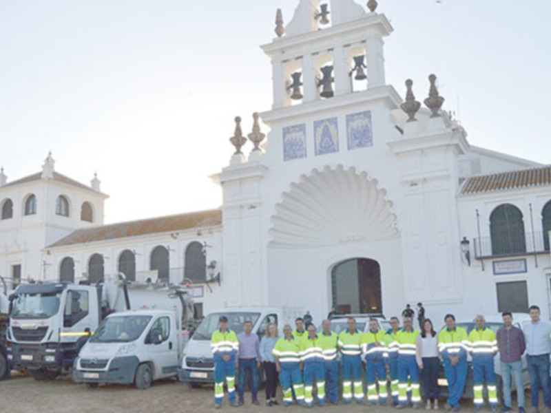 Equipo de trabajadores en uniforme frente a una iglesia blanca con camiones de servicio en el entorno.