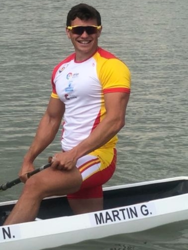 Atleta de remo en acción, vestido con traje rojo y blanco, remando en un barco con el nombre 'MARTIN G.' en la proa.