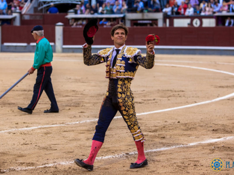 Un torero en su traje tradicional, celebrando con un sombrero en la mano, en una plaza de toros.