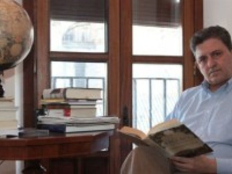 Hombre leyendo un libro en un ambiente de estudio con una mesa llena de libros y un globo terráqueo en el fondo.