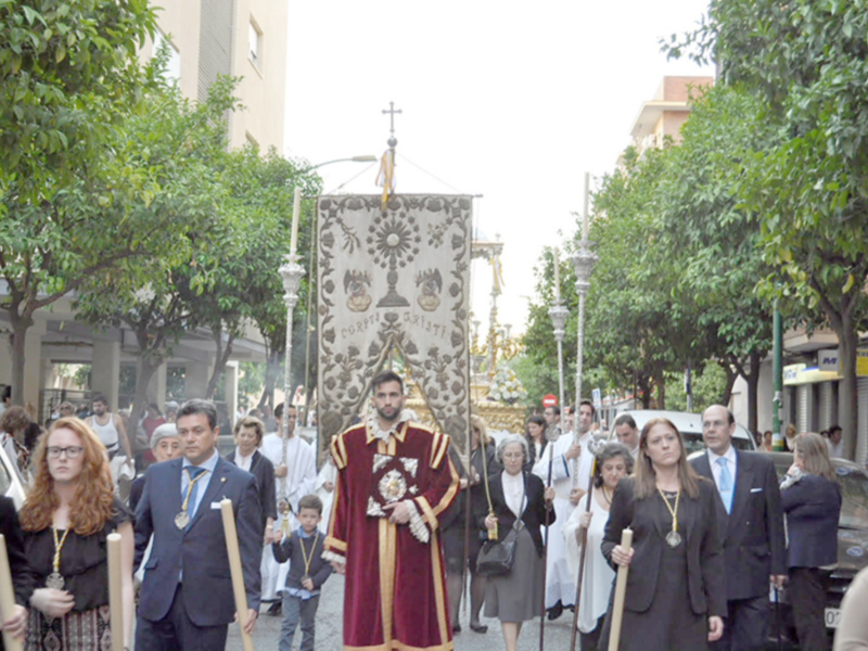 Procesión religiosa con portadores de estandartes y sacerdotes en una calle urbana.