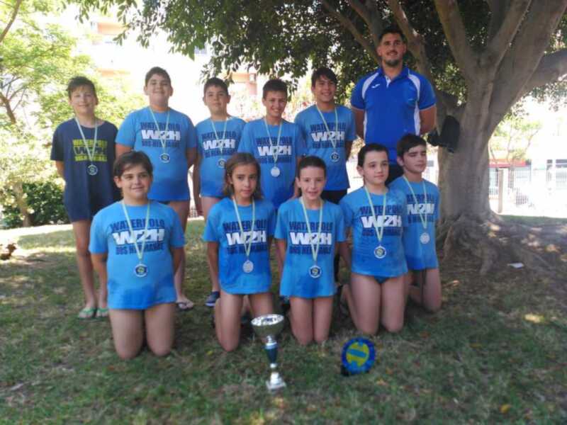 Equipo de Waterpolo celebrante con sus medallas y trofeo en un parque, posando orgullosamente en una imagen de equipo deportivo.