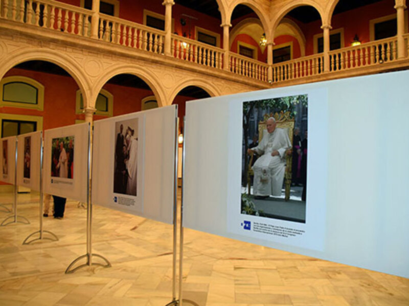 Exposición de fotografías en un patio histórico con arcos y balcones.