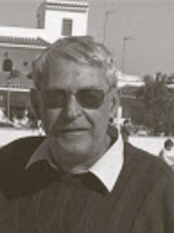 Retrato blanco y negro de un hombre con gafas de sol, posando al aire libre con un edificio en el fondo.