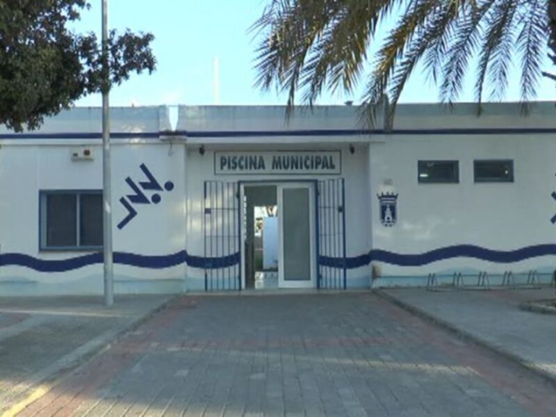 Piscina Municipal, edificio blanco con detalles azules y palmeras, ubicado en un entorno tranquilo.
