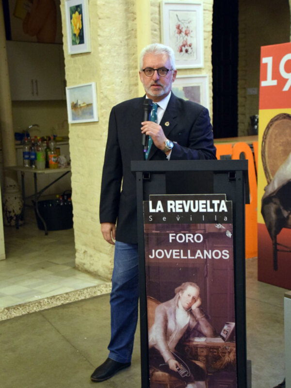Hombre hablando en un foro sobre 'La Revuelta Jovellanos' en Sevilla.