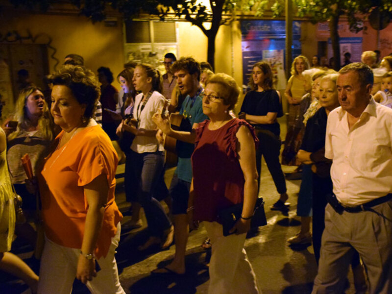 Una multitud de personas en una calle nocturna, con algunos de ellos usando gafas de sol y otros con bolsos. La escena parece ser una celebración o una reunión social en una ciudad.